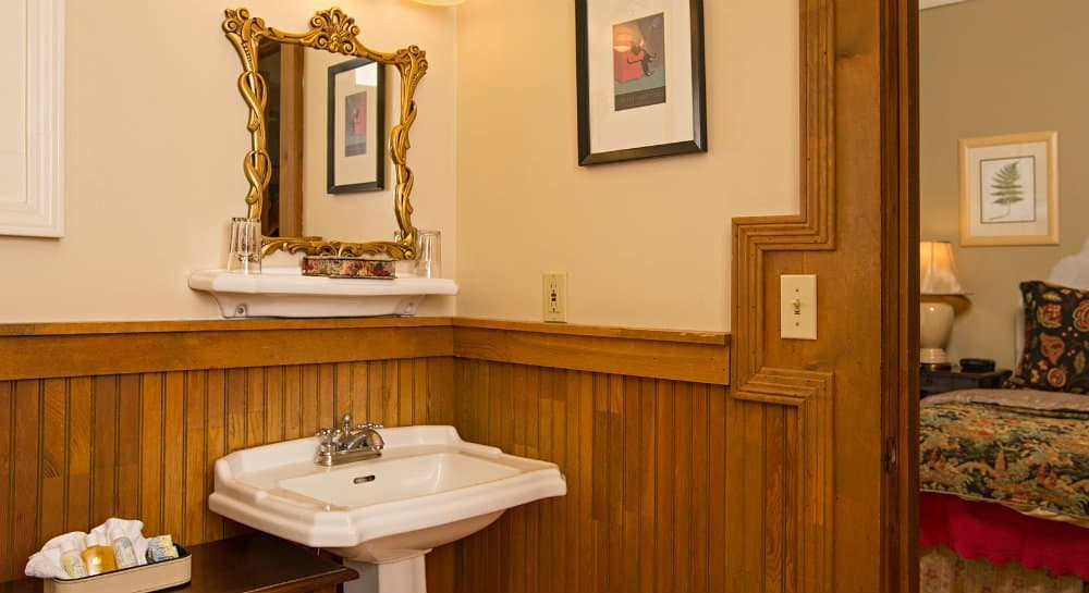 A vintage bathroom featuring a white sink, ornate mirror, and wooden paneling.