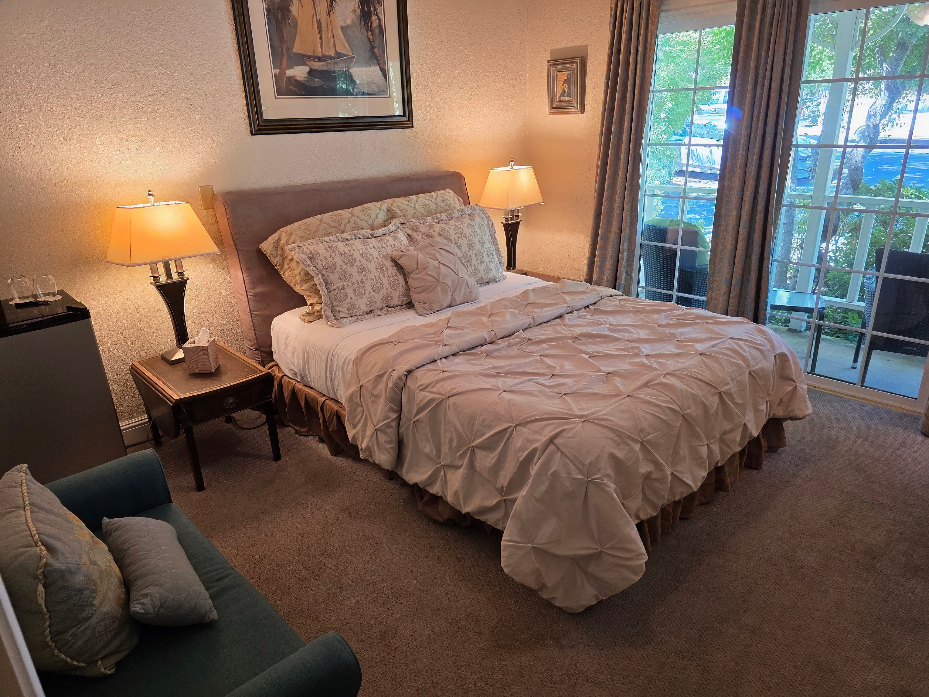 Cozy bedroom with a neatly made bed, two lamps, and a small sitting area by a window.