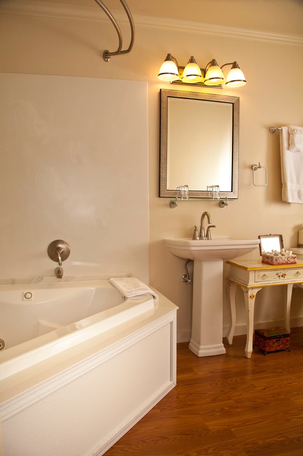 A well-lit bathroom featuring a soaking tub, sink, mirror, and decorative furniture.
