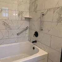 A clean, modern bathroom featuring a bathtub with marble-patterned tiles and grab bars.