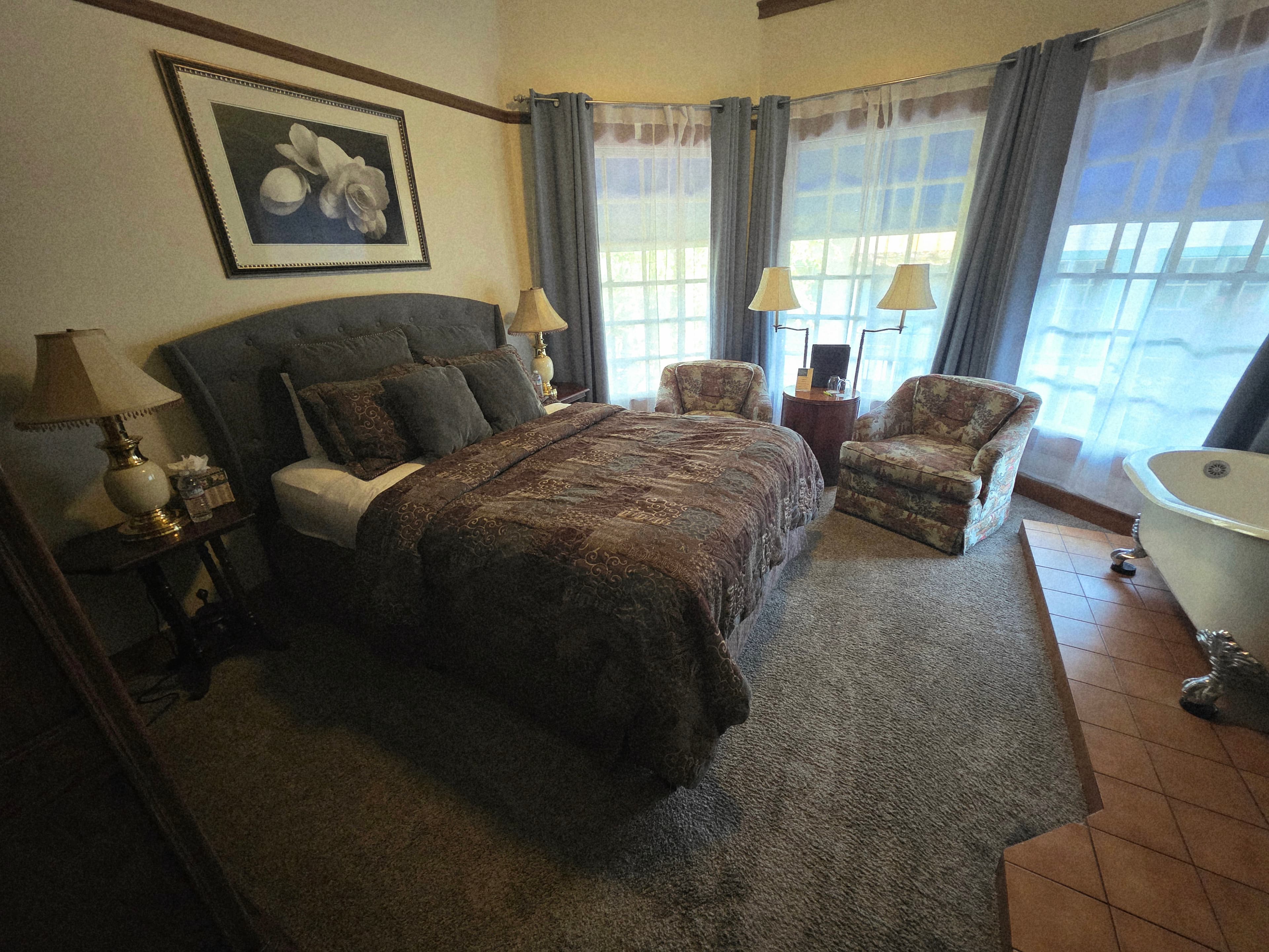 Cozy bedroom featuring a double bed, two armchairs, and large windows with soft drapes.