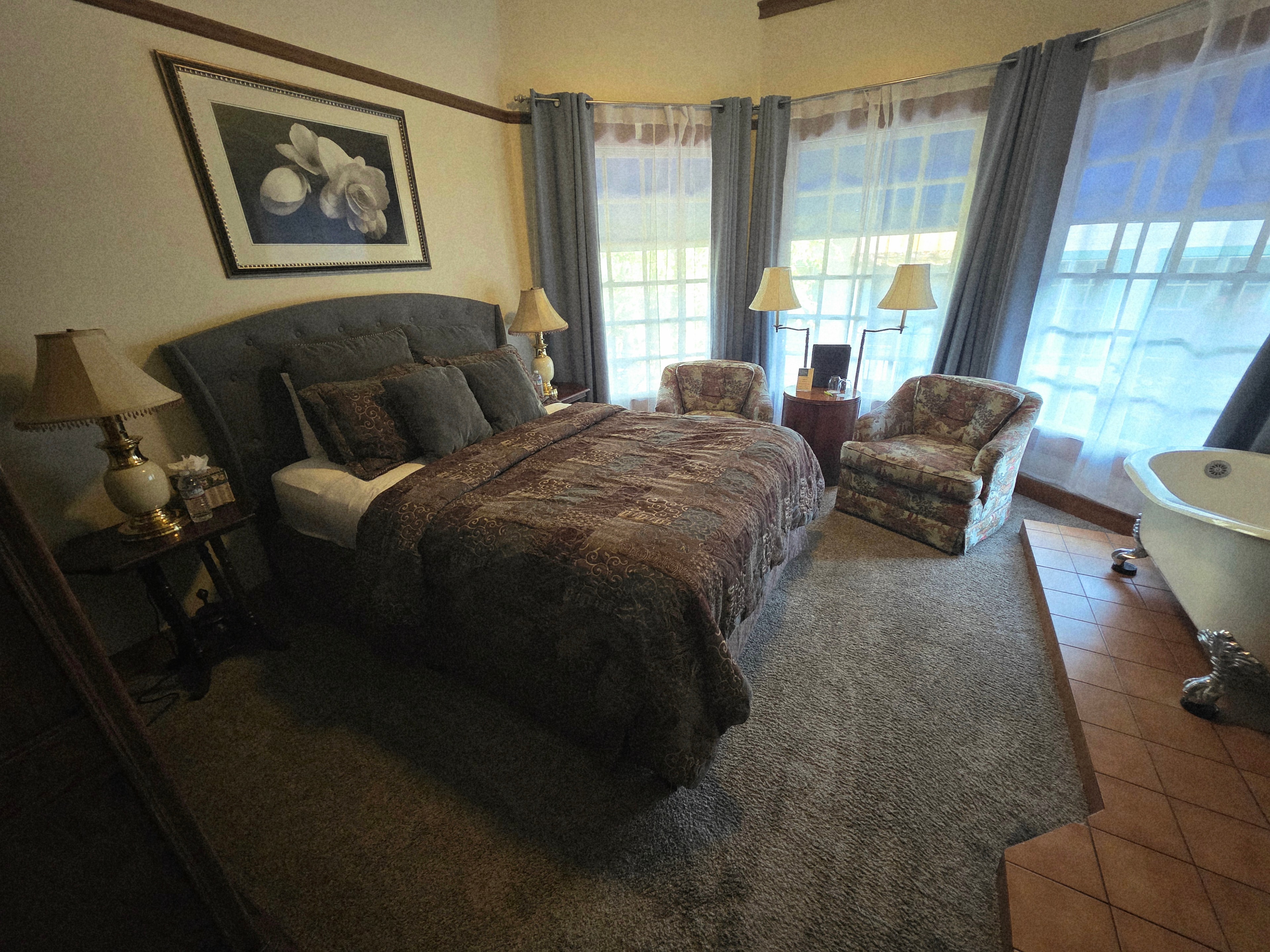 Cozy bedroom featuring a double bed, two armchairs, and large windows with soft drapes.