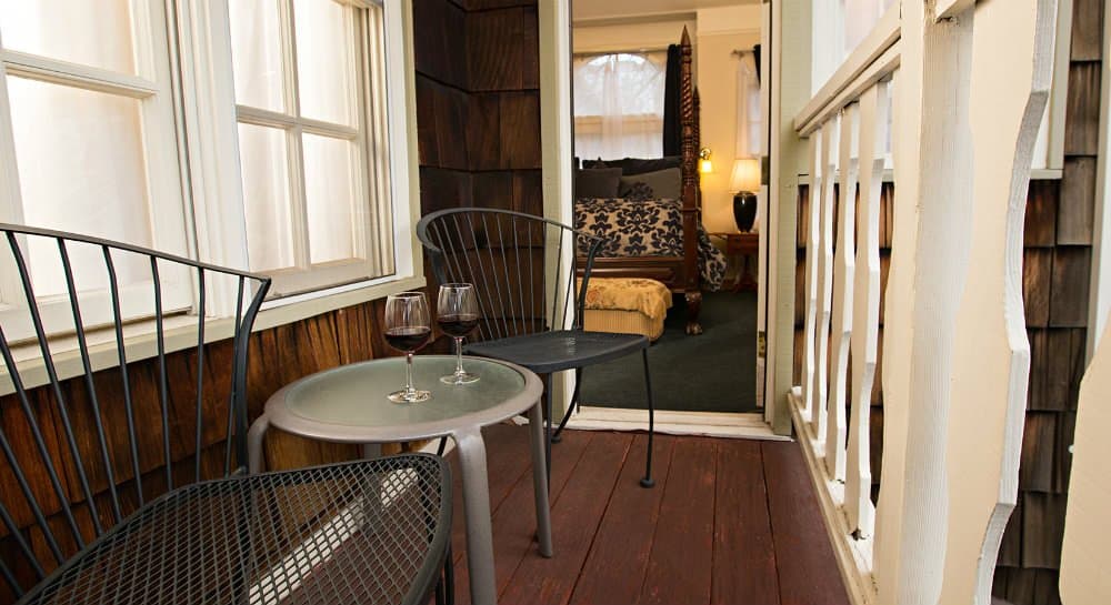 A cozy porch with two metal chairs and a small table holding two glasses of wine, leading to an inviting room.