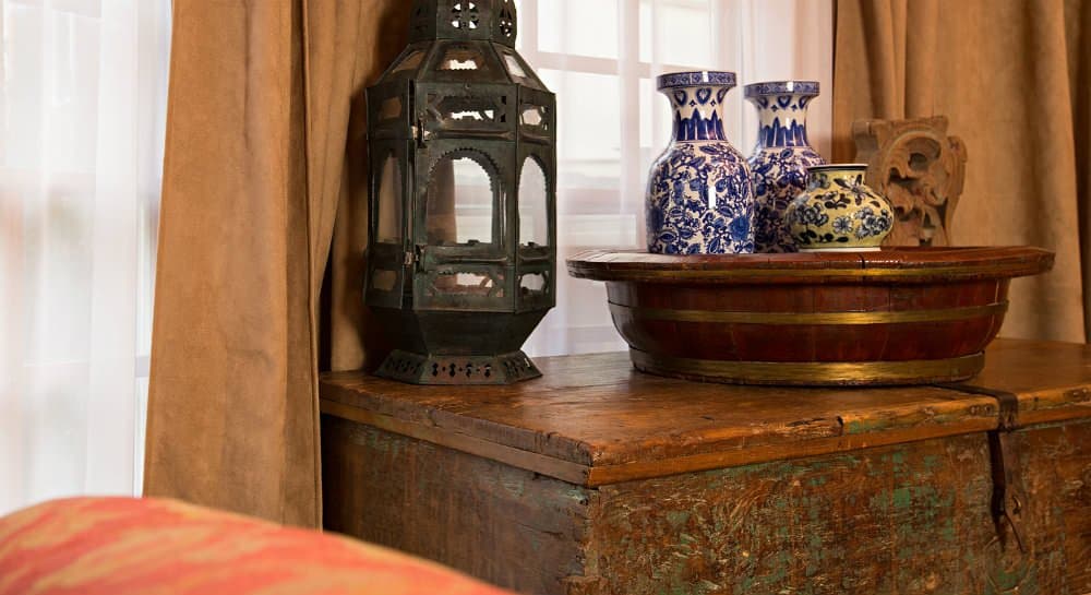 Decorative items, including a lantern and blue-patterned vases, on a wooden table with brown curtains in the background.
