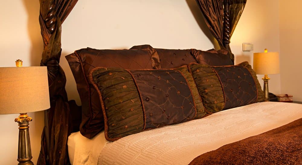 A cozy, elegantly decorated bed with rich brown and green pillows, flanked by stylish lamps.