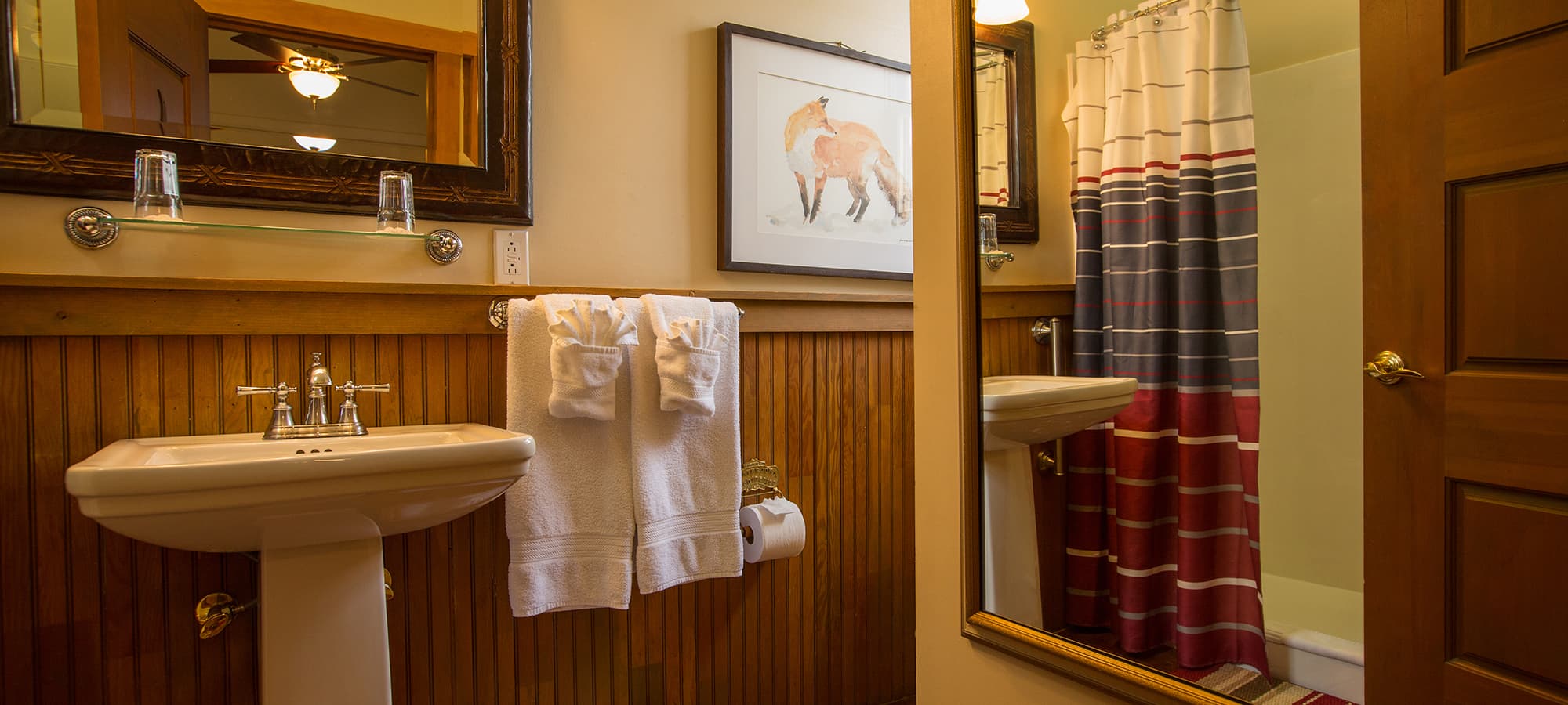 A cozy bathroom featuring a pedestal sink, towels, a shower curtain with stripes, and a framed artwork of a fox.