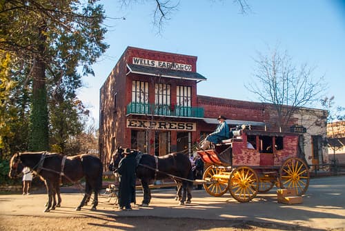 A horse-drawn stagecoach stops outside the Wells Fargo building in a historic town setting.