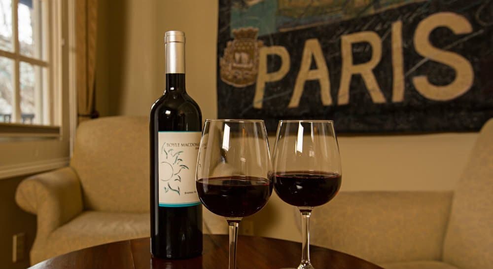 A bottle of red wine and two glasses sit on a wooden table against a backdrop with the word "PARIS."