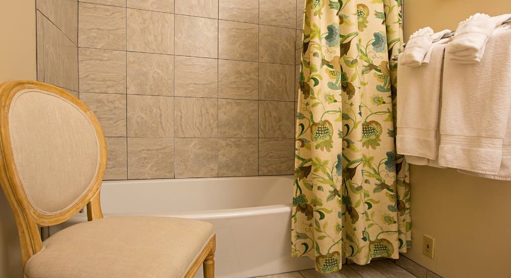 A bathroom featuring a bathtub, floral shower curtain, a chair, and neatly stacked towels.