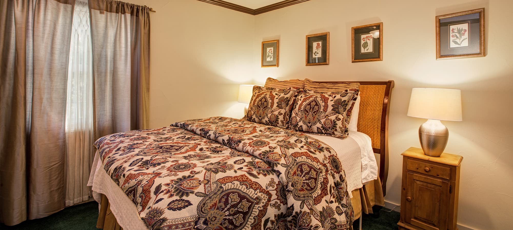A cozy bedroom featuring a bed with patterned bedding, bedside lamp, and framed artwork on the walls.
