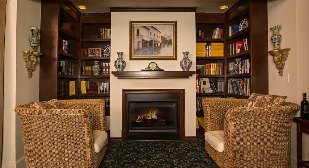 Cozy reading nook featuring two wicker chairs, a fireplace, and shelves lined with books and decorative items.