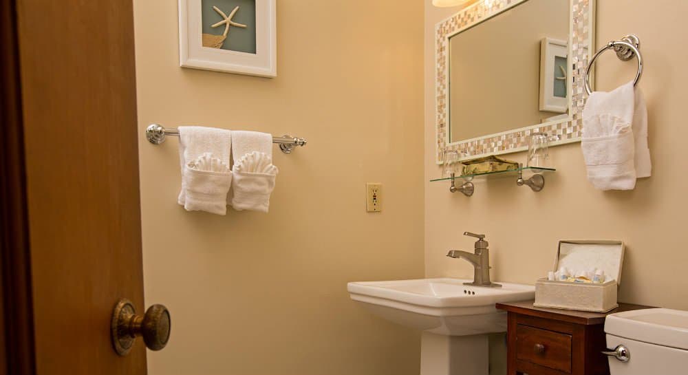 A small bathroom featuring a sink, mirrored wall, decorative towels, and a wooden cabinet.