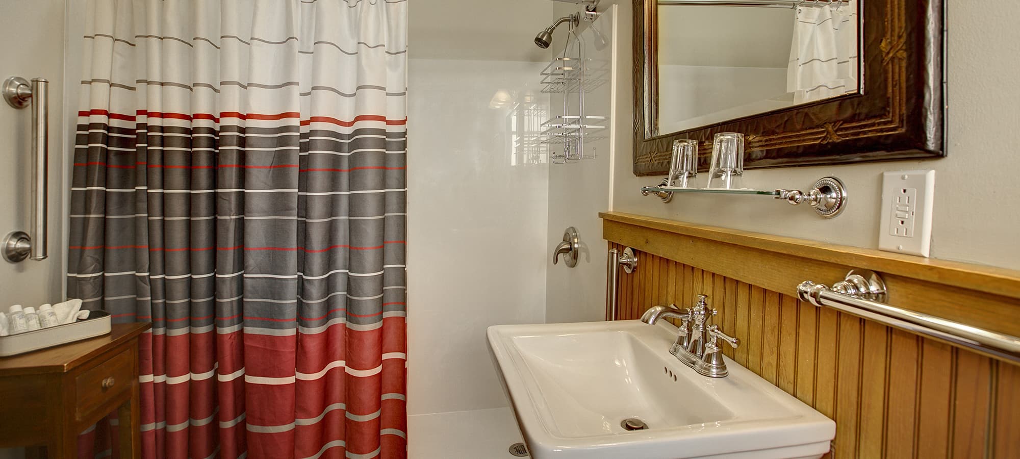 A modern bathroom featuring a striped shower curtain, a white sink, and wooden accents.