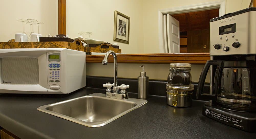 A kitchen corner featuring a microwave, coffee maker, sink, and countertop storage.