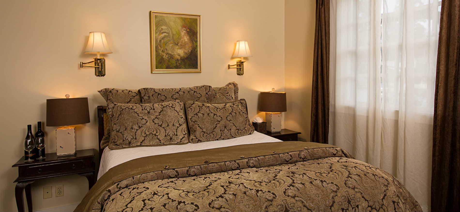A cozy, elegantly decorated bedroom featuring a large bed with ornate bedding, bedside lamps, and a window with sheer curtains.