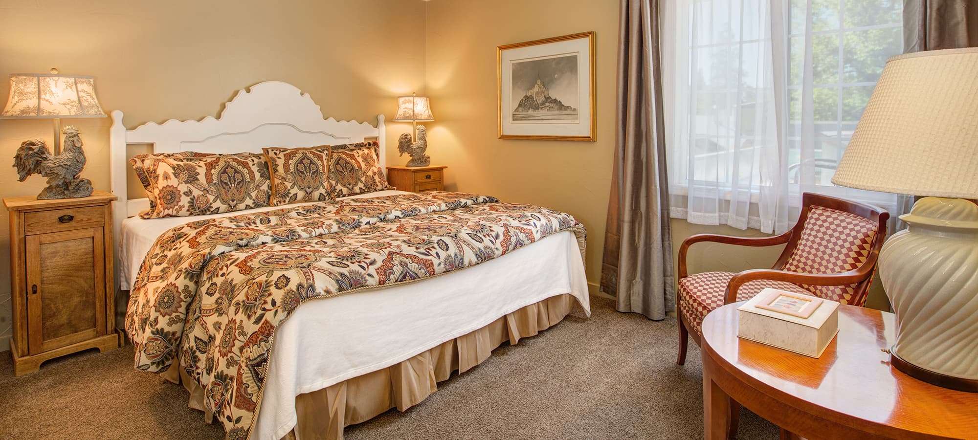 Cozy bedroom featuring a large bed with patterned bedding, a wooden nightstand, and warm lighting.