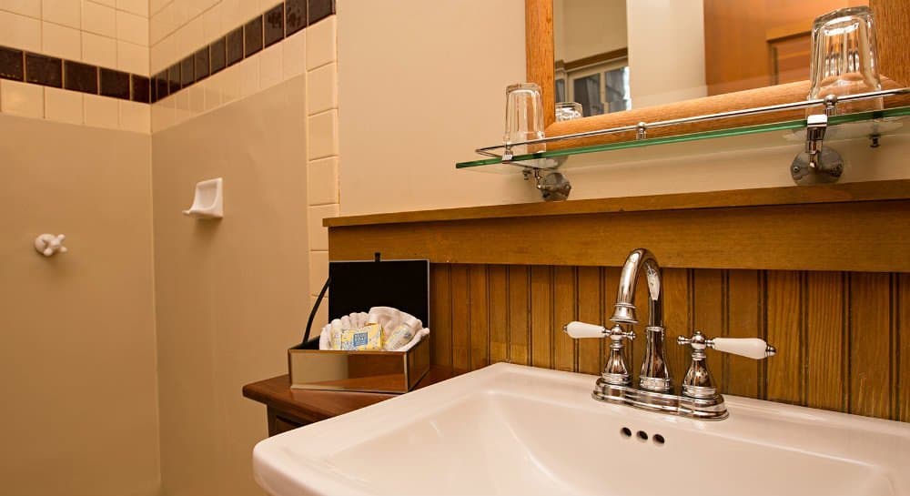 A modern bathroom featuring a white sink with silver faucets, a wooden accent wall, and toiletries neatly arranged nearby.