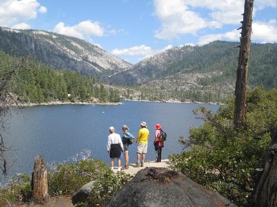 Four hikers stand by a tranquil lake surrounded by mountains and trees.