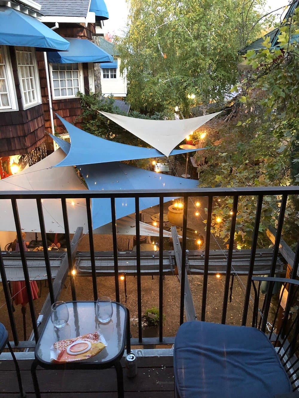 A cozy outdoor seating area with blue canopies and string lights viewed from a balcony.