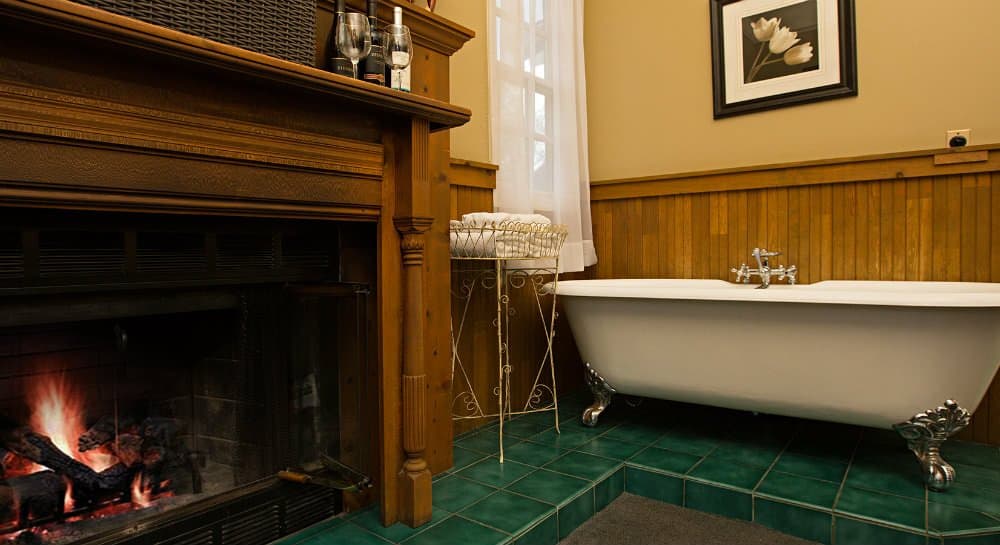 A cozy bathroom featuring a vintage clawfoot tub next to a fireplace and wooden accents.