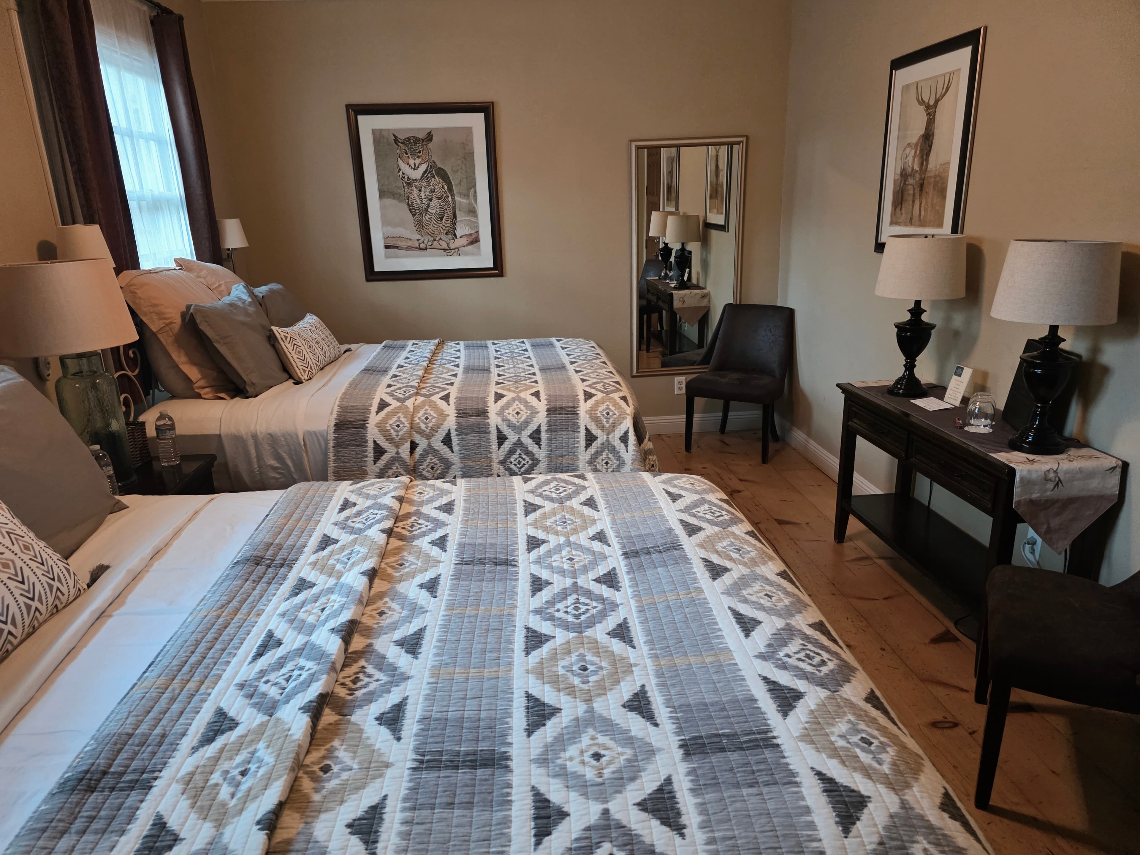 A cozy guest room featuring two beds with patterned quilts, a chair, and decorative art on the walls.