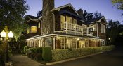 Exterior of inn at dusk with cedar shake siding and white trim, lit windows surrounded by trees and manicured shrubs