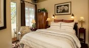 ivory bedroom with white comforter and pillow, picture over, three stands with lamps, brown curtains with sheer, hutch