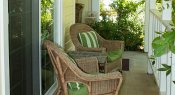 Covered patio with white railing, two wicker chairs with green cushions and green and white striped pillows