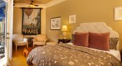 bedroom with tan colored paisley comforter, red pillows, night stand with lamp, pictures on wall and Paris Banner