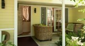Covered patio with two wicker loveseats with green and white cushions in front of a partially open French door