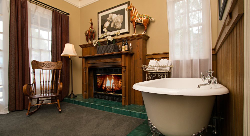 Tan room and fireplace with wood mantle surround, a wood rocking chair, and white freestanding tub
