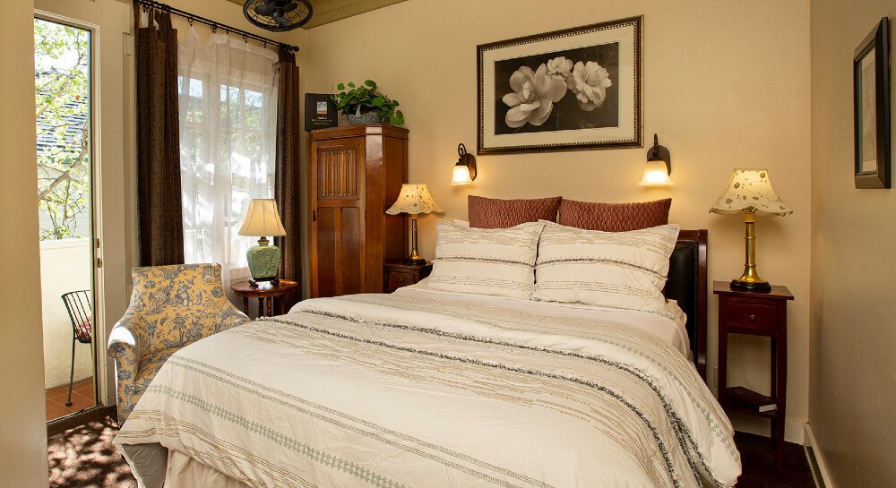 Bed with white comforter and pillows, ivory walls, floral picture and two sconces over bed, two nightstands with lamps