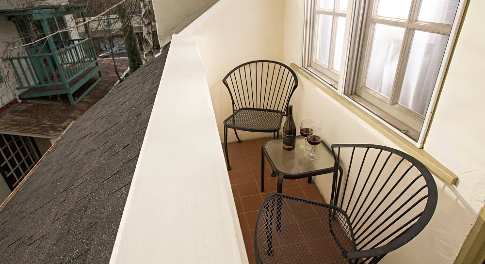 Overview of balcony with black metal chairs and table with wine bottle and two glasses of red win