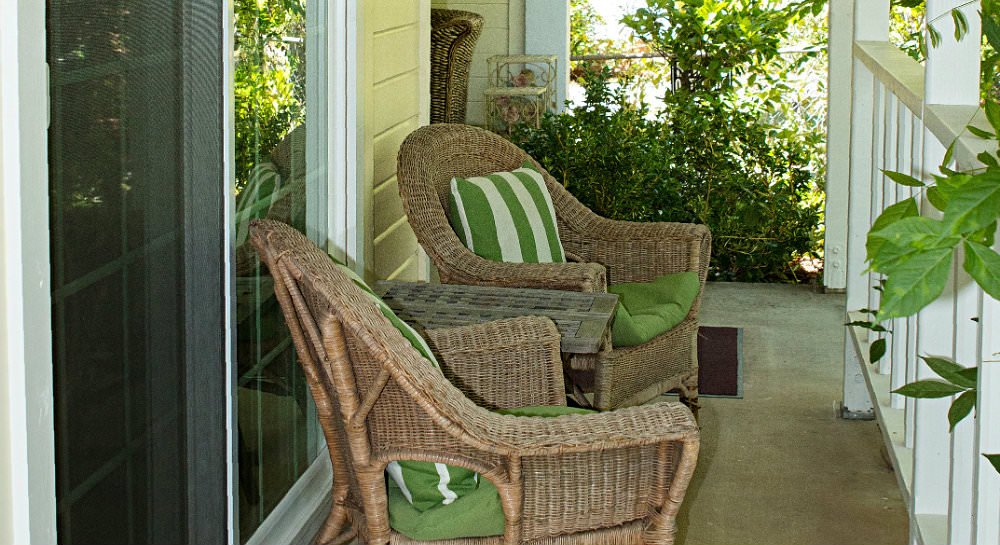 Covered patio with white railing, two wicker chairs with green cushions and green and white striped pillows