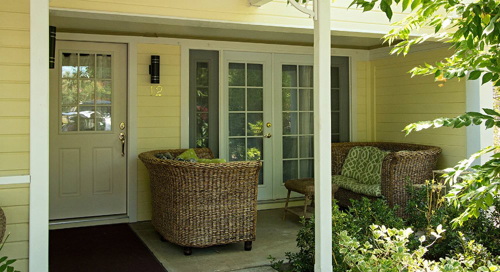 Covered patio with two wicker loveseats with green and white cushions in front of a partially open French door