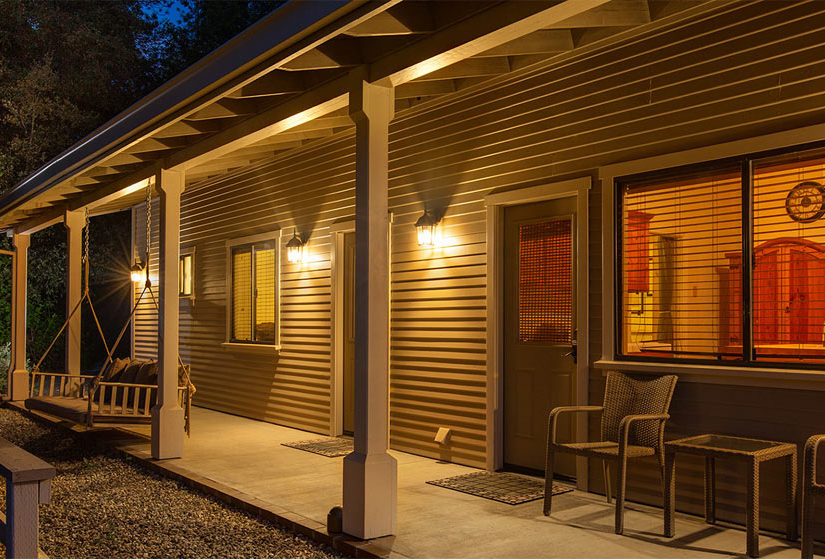 Night time view of cottage entry and through window, with porch swing hanging near the door.