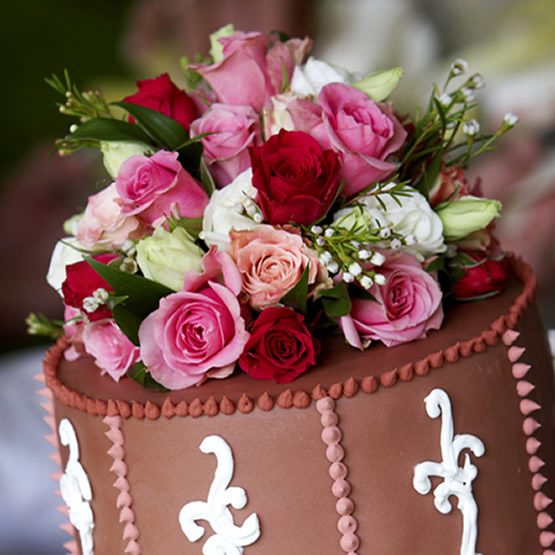 Frosted cake topped with a bouquet of red, pink, peach, and white flowers and greenery