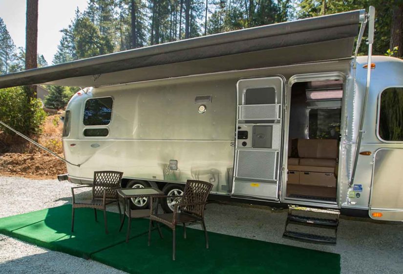 An outdoor bistro set sits on green astroturf in front of the old metal airstream rv