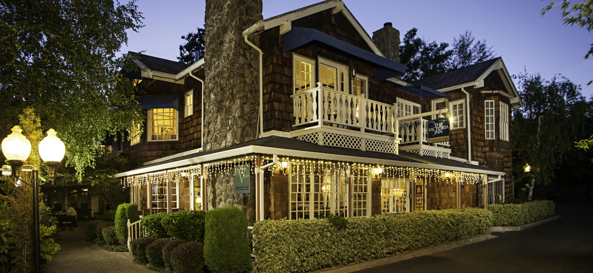 Victoria Inn exterior at dusk with warmly lit windows surrounded by lush green trees and manicured shrubs