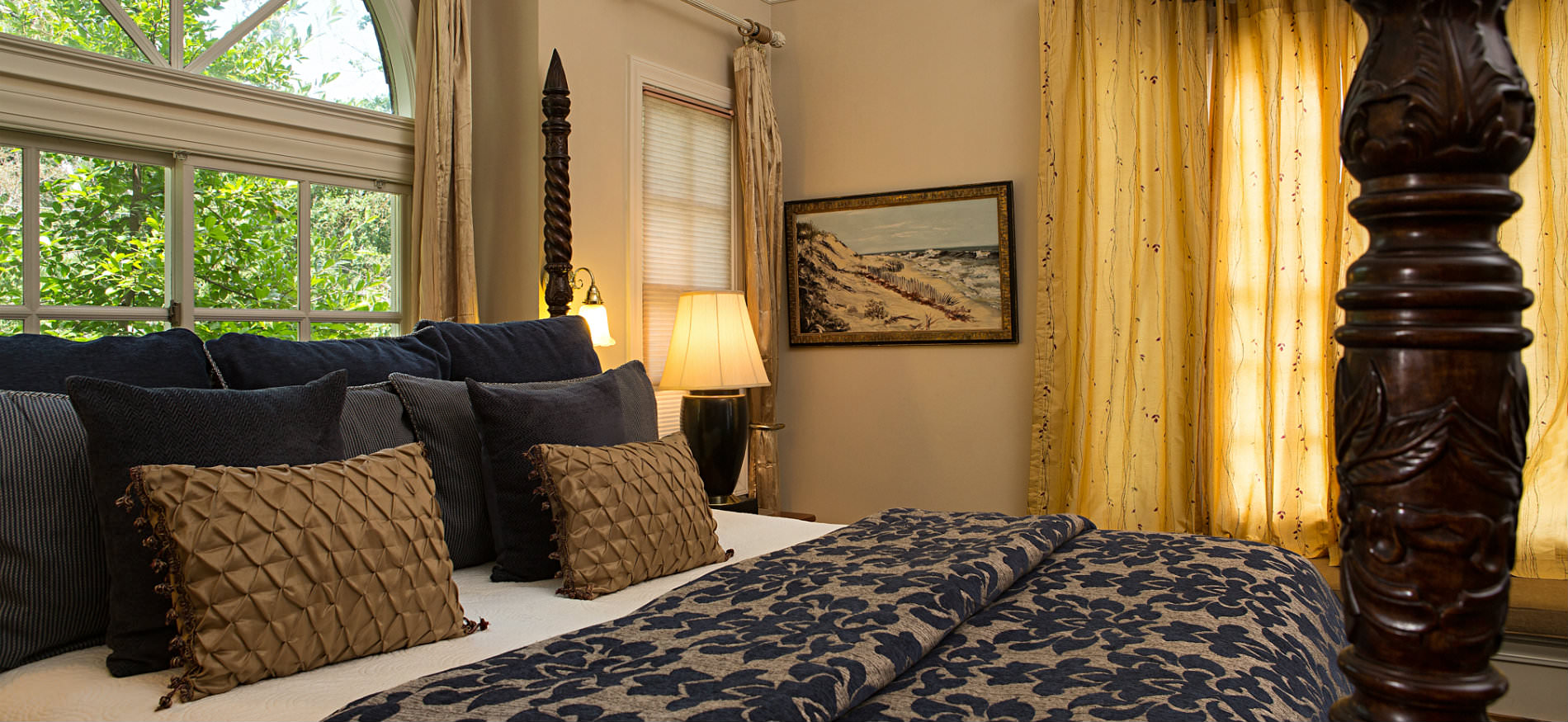 Warm cozy bedroom decorated in black, brown, tan and gold with four poster bed and arch top window