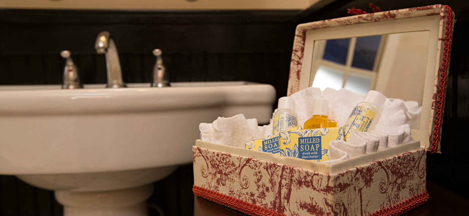 Close up view of small red and white toile box opened with mirror inside and sample sized toiletries