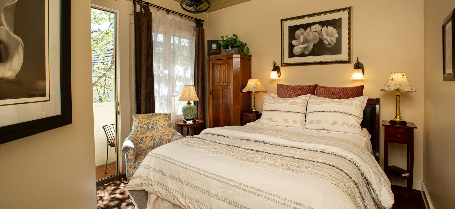 Bed with white comforter and pillows, ivory walls, floral picture and two sconces over bed, three nightstands with lamps