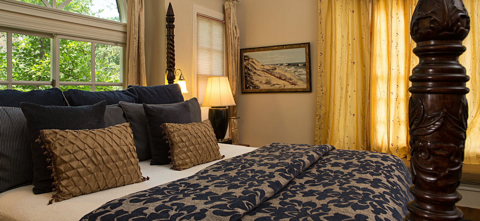 Warm cozy bedroom decorated in black, brown, tan and gold with four poster bed and arch top window