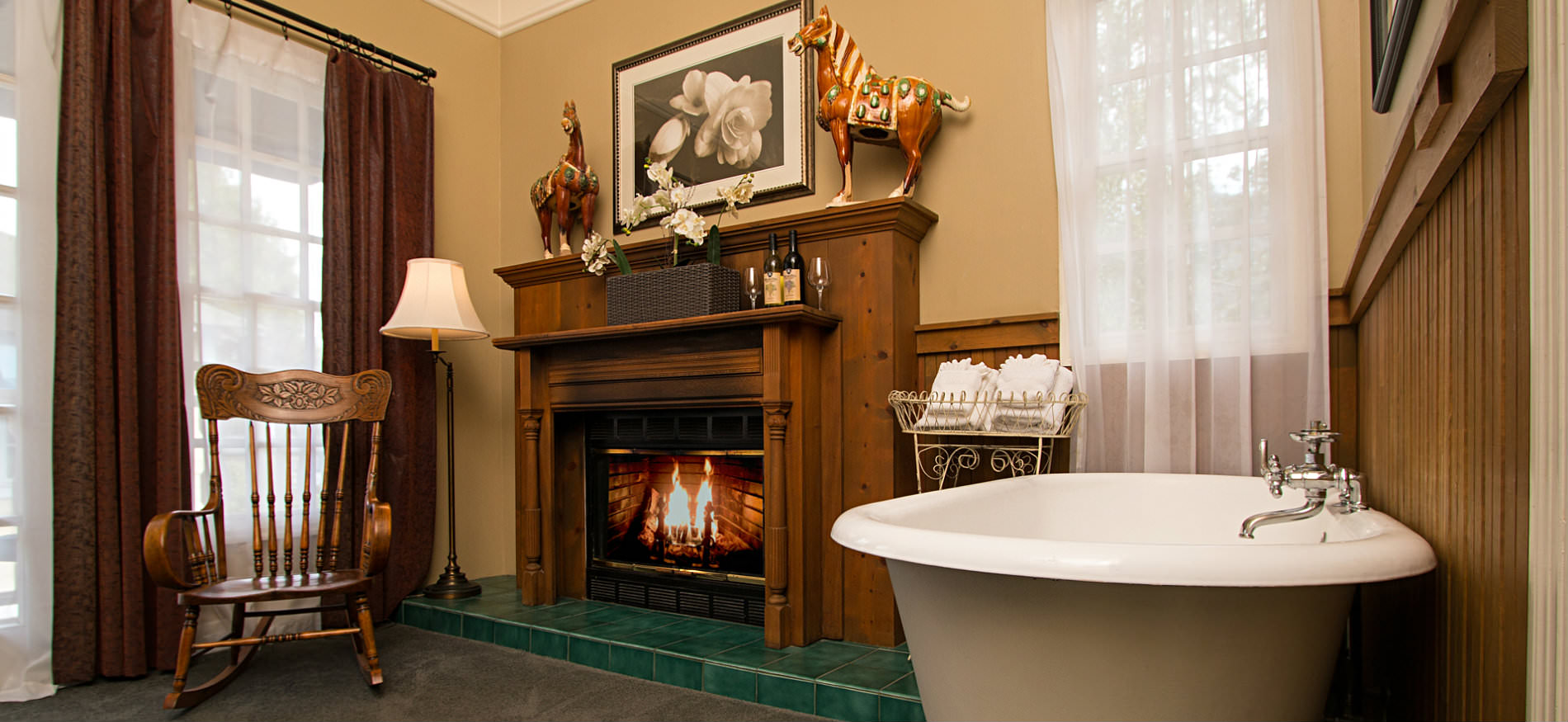 Tan room and fireplace with wood mantle surround, a wood rocking chair, and white freestanding tub