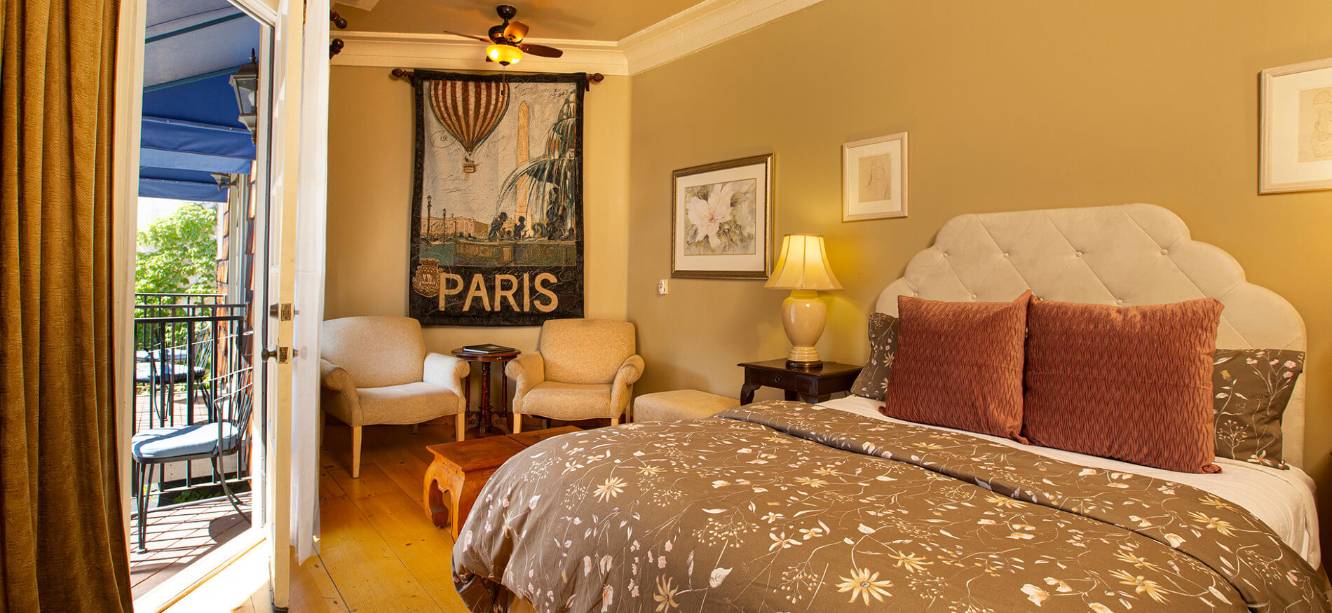 cream and yellow bedroom with tan colored comforter, red pillows, night stand with lamp, pictures on wall and Paris Banner hanging