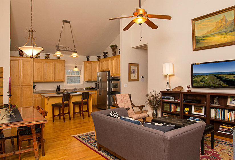 living room with tv on wall over shelves with celing fan, dining table on hardwood floors, kitchen with bar area with a lot of oak cabinets, stainless steel appliances