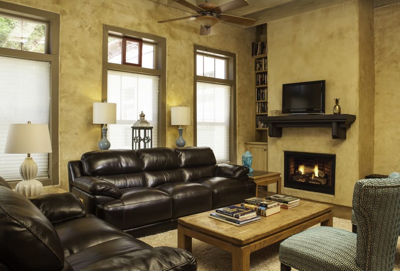 Living room with gold walls, brown leather furniture, a fire in the fireplace and three windows topped with transom windows