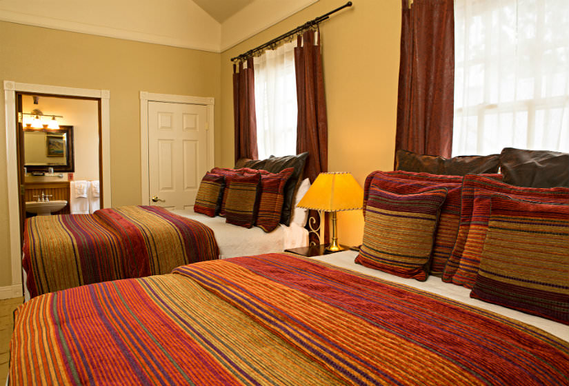 Bedroom with two beds covered in red and gold striped bedspreads, a nightstand, and two large windows