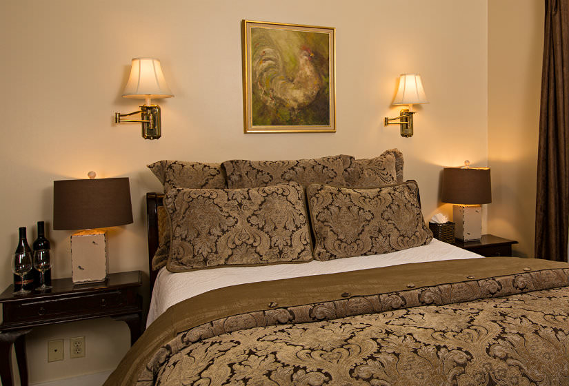 Brown and black pillows and comforter on bed, two nightstands with lamps, two sconces and framed rooster print over bed