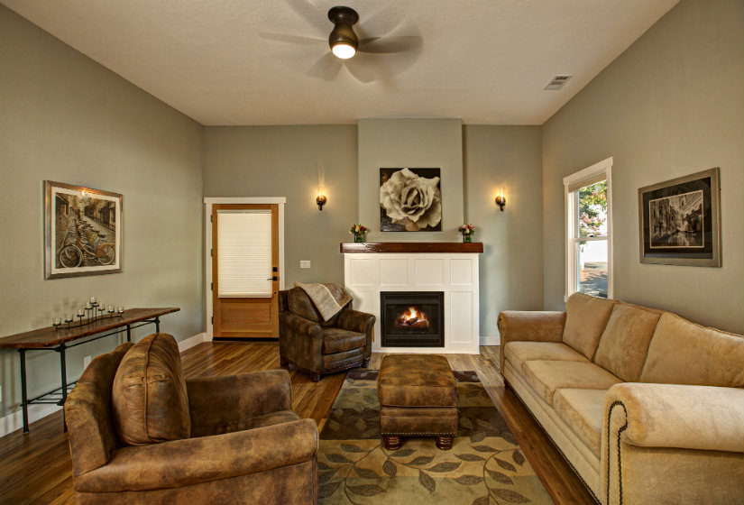 Sage green living room with wood floors a couch with two chairs and a warm fire in the fireplace